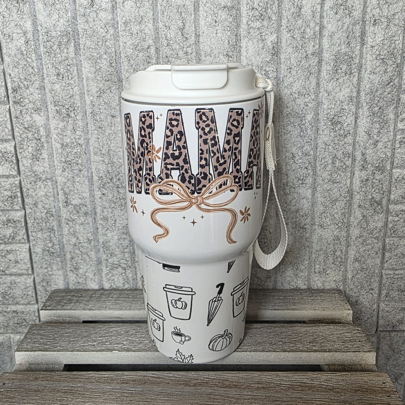 White tumbler with decorative design on a wooden surface against a tiled wall.