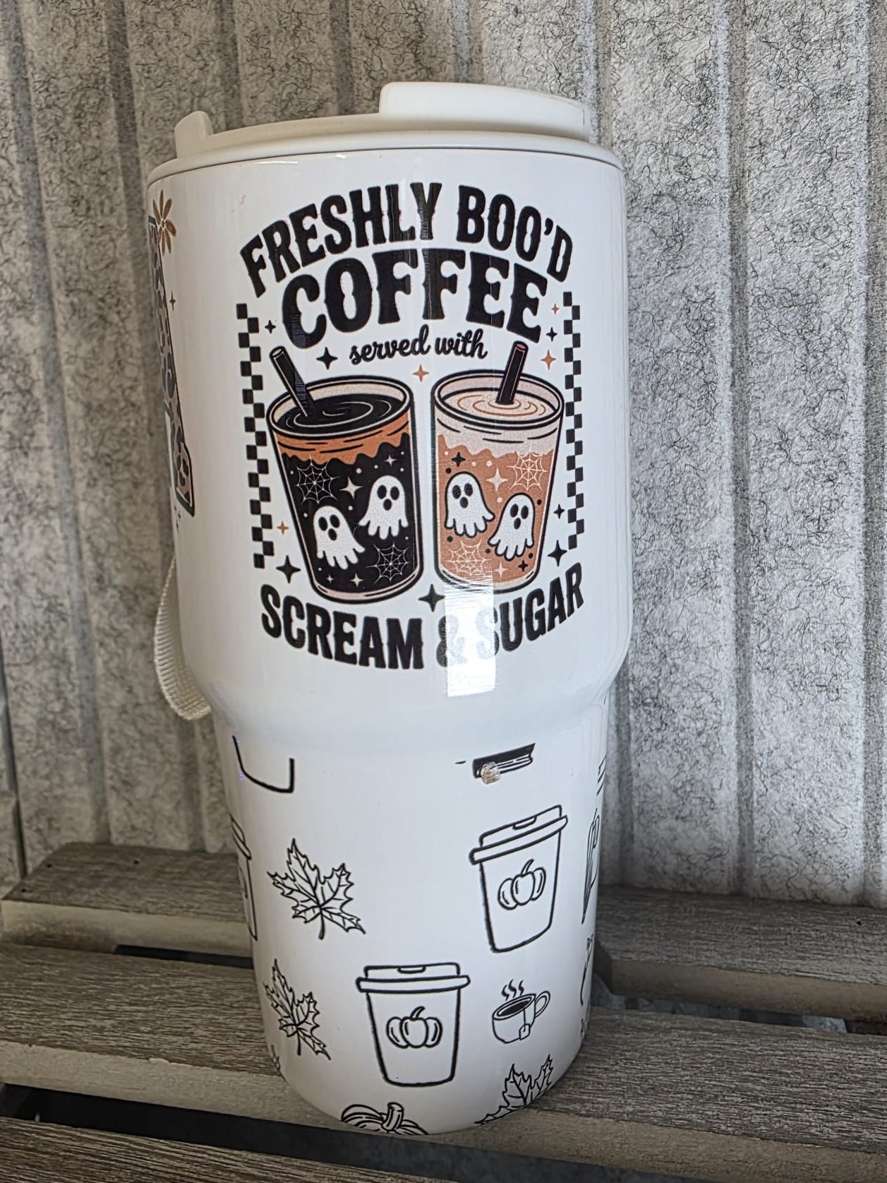 Tumbler with Halloween-themed coffee design on a wooden surface.